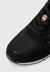 Sneaker nera con una combinazione di suede e tessuto testurizzato, dettagli lucidi e un design con lacci con elementi metallici.