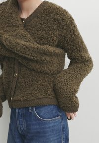 Bruine, gestructureerde cardigan met een pluizig oppervlak, V-hals en knoopsluiting. Gecombineerd met blauwe denim jeans met een klassieke pasvorm.