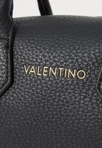 Črna usnjena torbica z teksturirano površino. Vsebuje zlato obarvan "Valentino" logotip. Oblika vključuje dve zgornji ročici in ostre robove.