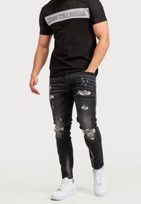 Černé tričko s nápisem "KINGS WILL DREAM" v šedé barvě přes hrudník, doplněné o roztrhané černé skinny džíny a bílé tenisky.