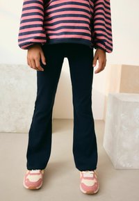 Marineblå bukser med flagrende ben og ribbet tekstur, parret med pink og cremefarvede sneakers med gule accenter. En stribet langærmet bluse er også synlig.
