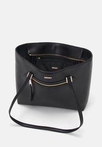 Black leather tote bag with a smooth texture, featuring gold hardware, zippered pockets, and a spacious interior. Brand logo displayed inside.