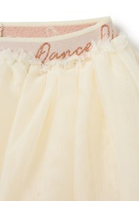 Crèmekleurige tule rok met gegatherde lagen en een zachte textuur. Elastische tailleband met het woord "Dance" in roségouden borduursel.