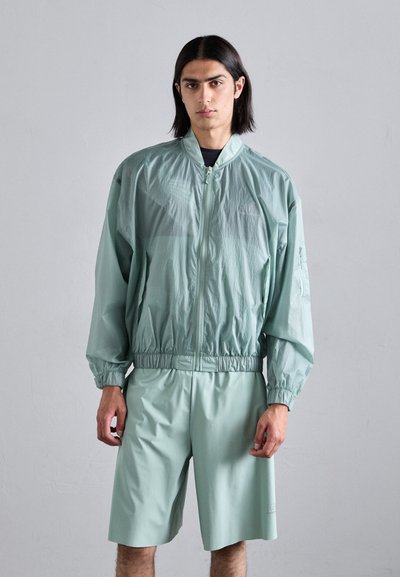 Lichte mintgroene jas met elastische manchetten en tailleband, gecombineerd met bijpassende shorts. Glad textuur en minimale ontwerpelementen.