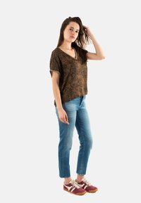Top marrón de cuello en V con un patrón texturizado y mangas enrolladas, combinado con jeans azules claros y zapatillas burdeos con acentos en crema.