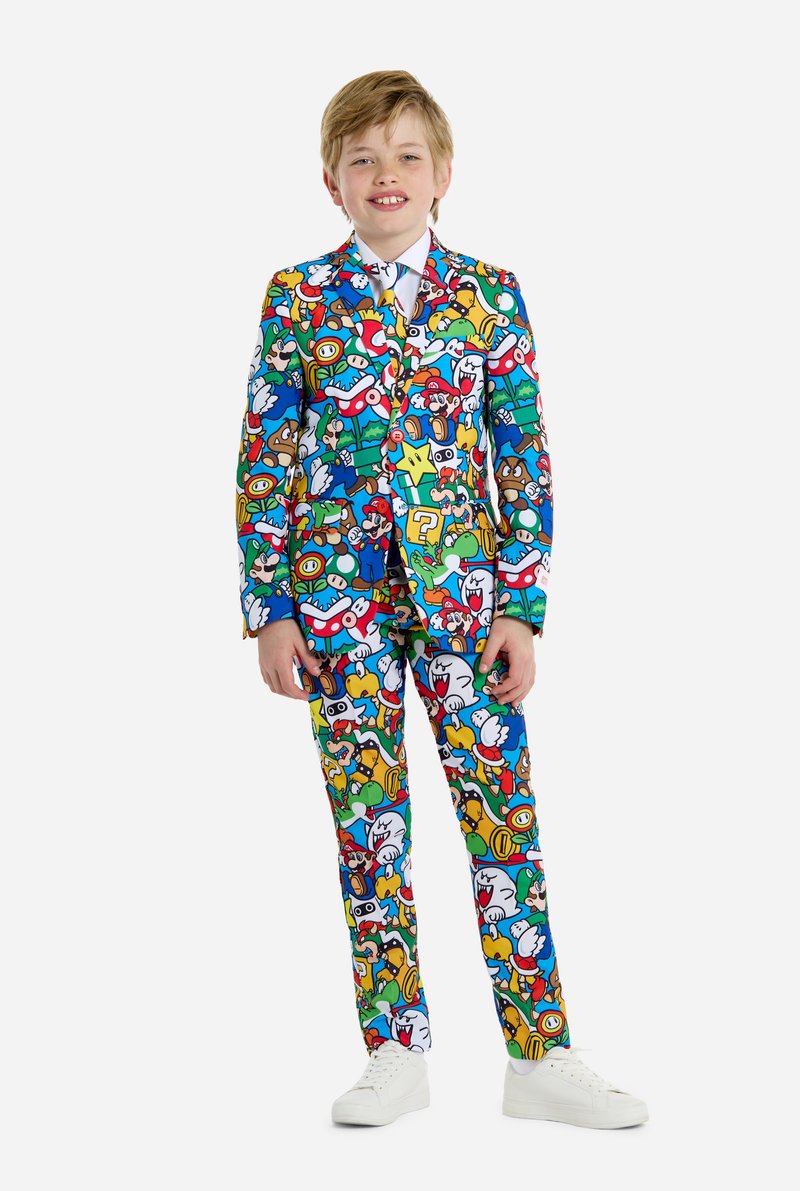 Bunter Kinderanzug mit einem vollständigen Muster von Cartoonfiguren, hauptsächlich in Blau, Rot, Grün und Gelb. Weißes Hemd und Schuhe.