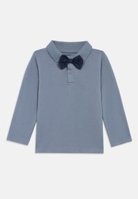 Ανοιχτό μπλέ μακρυμάνικη μπλούζα πόλο με ναυτικό μπλέ παπιγιόν συνημμένο στο κολάρο, τοποθετημένο επίπεδα σε λευκό φόντο.