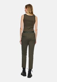Dark olive green sleeveless top paired with matching tapered pants featuring a patterned waistband and slits at the hem, complemented by black boots.