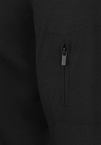 Zwart gebreid stof met een ritszak aan de zijkant. De structuur is glad en consistent, wat het functionele ontwerp benadrukt.