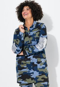 Camisa de camuflaje en azul, verde y negro con parches de codo de lentejuelas plateadas, cierre de botones, bolsillos y cuello.