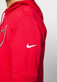 Hoodie Nike rouge avec un logo blanc sur la manches gauche et un design sportif. Texture lisse avec une poche avant et une capuche à cordon.
