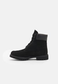 Botas de tobillo de ante negro con suela de goma, puntera redonda y frente con cordones. Cuenta con un cuello acolchado y paneles texturizados para mayor agarre.