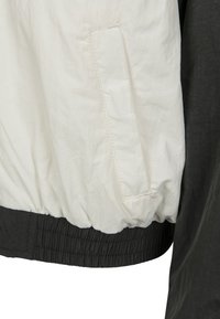 Vit och mörkgrå jacka med ett strukturerat, lättviktsmaterial, elastisk midja och en sidoficka med sömdetaljer.