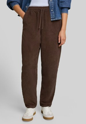 Person wearing brown corduroy jogger pants with drawstring waist, white sneakers, white top, and cropped blue denim jacket.