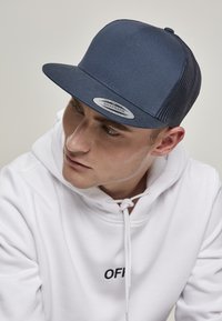 Casquette snapback navy avec un design structuré, un panneau avant solide, des côtés en maille et un écusson de logo brodé à l'avant. Associée à un sweat à capuche blanc.