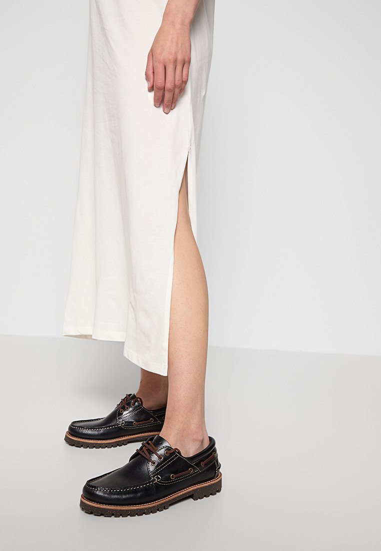 Zwarte leren schoenen met bruine accenten, veters en gewatteerde zolen, gecombineerd met een lange, crèmekleurige jurk met een zijsplit.