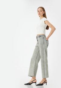 Witte korte mouwen crop top gecombineerd met hoog-waist, wijde grijze jeans met een rafelrand, aangevuld met zwarte slingback hakken.