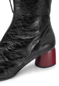 Stivaletto alla caviglia in pelle nera con una texture screpolata e un distintivo tacco a blocco rosso. Presenta una cerniera laterale per la chiusura.