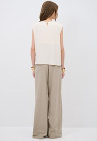 Top sin mangas de color crema con un detalle de abertura en la parte posterior, combinado con pantalones de pierna ancha de color beige claro. Diseño minimalista, textura suave.