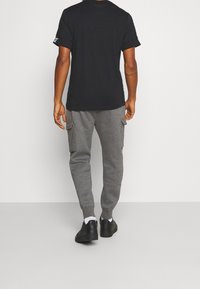 Svart kortärmad t-shirt i kombination med grå cargobyxor av sweatpants-typ. Byxorna har sidfickor och ribbade mudd; bärs med svarta sneakers och vita strumpor.