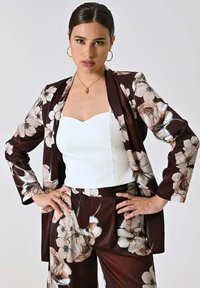 Blazer marrone a fantasia floreale con pantaloni coordinati e top bianco senza spalline. Presenta accenti floreali chiari e scuri. Tessuto dalla consistenza liscia.