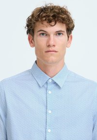 Cămașă bleu deschis cu model geometric, din bumbac, cu guler întins și nasturi albi. Textură netedă și croială ajustată.