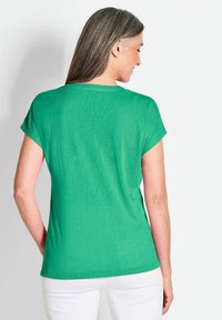 Groen T-shirt met korte mouwen en een ronde halslijn, met een zachte textuur, gezien van achteren tegen een witte achtergrond.
