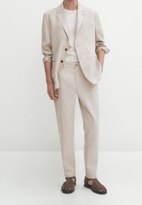 Khakifärgad linnblazer med två knappar, matchande byxor och en vit t-shirt. Bruna, vävda lädersandaler fulländar outfiten.