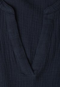 Gros plan sur un tissu texturé bleu marine foncé présentant un décolleté en V avec des bords de col pliés.