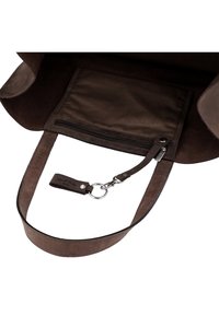 Interno di una borsa in pelle marrone che mostra una tasca con zip e un portachiavi attaccato con cinturino in pelle e clip metallica.