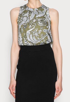 Blouse sans manches en vert olive avec des motifs floraux et paisley blancs. Encolure ronde simple, associée à une jupe noire ajustée.