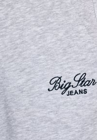 Šedé tričko se změkčenou texturou, na levém dolním rohu s námořnickou modrou vyšitou textem "Big Star JEANS" psaným kurzívou.