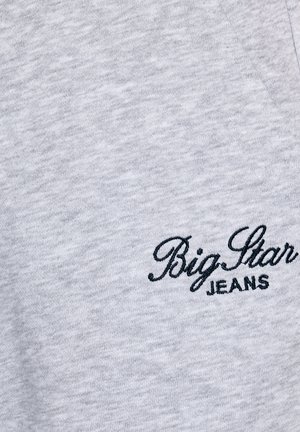 Pelēka T-krekls ar mīkstu tekstūru, kuram apakšējā kreisajā pusē ir izšūts tumši zils teksts "Big Star JEANS" slīpā rakstā.