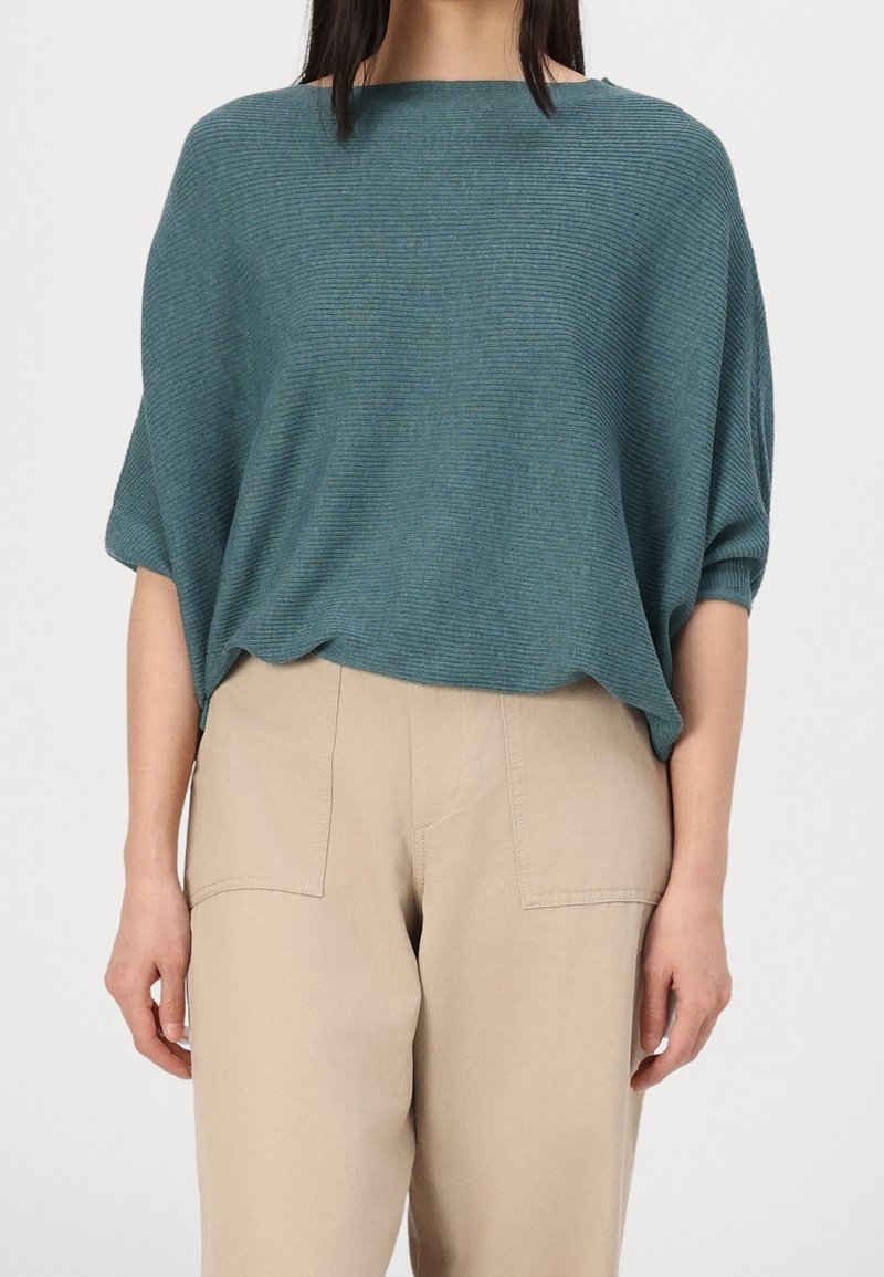 Teal kortärmad topp med avslappnad passform, ribbad textur och vid halsringning, matchad med ljusbeige, högmidjade byxor med framfickor.