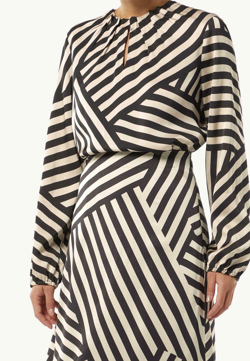 Femme portant une robe à manches longues avec des rayures diagonales géométriques noir et blanc et une petite fente au niveau de l'encolure devant.