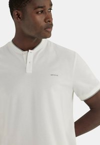Polo shirt bianco a maniche corte con colletto a bottoni. Presenta un bordo grigio e un logo discreto sul petto. Realizzato in tessuto morbido e liscio.