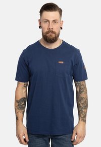 T-shirt in cotone blu navy con collo rotondo, maniche corte, taschino frontale e una patch in pelle con logo sul petto. Tessuto testurizzato.
