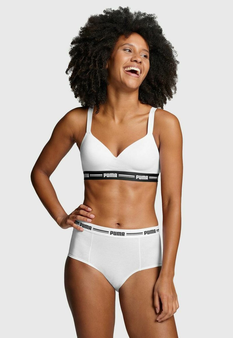 Weißer BH und hochgeschnittene Slips mit schwarzem Branding. Der BH hat ein V-Ausschnitt-Design und verstellbare Träger; die Slips verfügen über einen logoed Taillengummi.