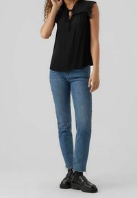 Top nero a maniche corte con scollo a chiave e dettagli a balze, abbinato a jeans blu a gamba dritta e stivali neri alla caviglia.