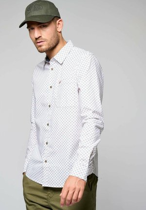 Witte overhemdo met een geometrische print in blauw, rood en groen. Stof lijkt lichtgewicht. Heeft een borstzak en lange mouwen.