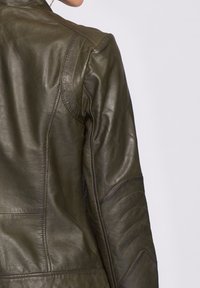 Olivgrön läderjacka med en slät yta, med snedställda sömmar och kviltade detaljer på axlarna och ärmarna.