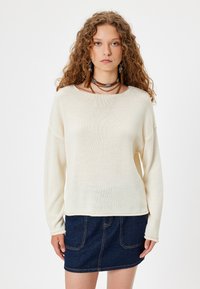 Maglione in maglia color crema chiaro con scollo ampio e maniche lunghe, abbinato a una gonna mini in denim scuro con cuciture visibili e tasche.