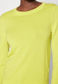 Bright yellow long-sleeve sweater made of smooth, lightweight fabric, featuring a crew neckline and ribbed detailing at the hem.