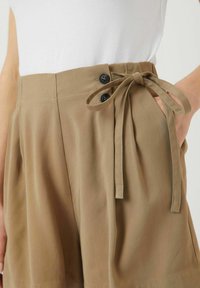 Ljust bruna shorts med hög midja, sidofickor, två svarta knappar och knytband i jämn utsmyckning.