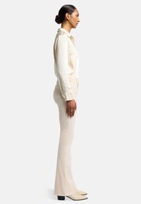 Crèmezijde shirt gestoken in lichtbeige flared pants, gecombineerd met beige puntige laarzen. Gladde textuur, aansluitend ontwerp en minimale accessoires.