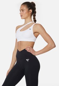 Witte sportbeha met een diagonale band en uitsnijdetails. Hoge zwarte leggings met een subtiel V-vormig ontwerp en logo.