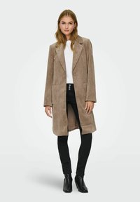 Brun kordtöjjacka med en lång, skräddarsydd design, framknappar och sidofickor, i kombination med svarta byxor och ankelstövlar.
