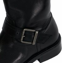 Botte noire en cuir montante jusqu'au genou avec une surface texturée, une boucle en métal argenté sur une sangle, et un talon noir légèrement surélevé.