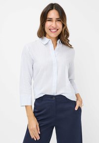 Light blue striped button-up shirt with three-quarter sleeves, made of a smooth fabric. Paired with dark navy pants, showcasing a casual fit.