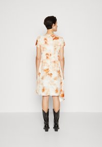 Rochie cu mânecă scurtă, cu un design fluid, având un model abstract în nuanțe de crem și portocalie, și o margine asimetrică. Asortată cu cizme negre până la gleznă.
